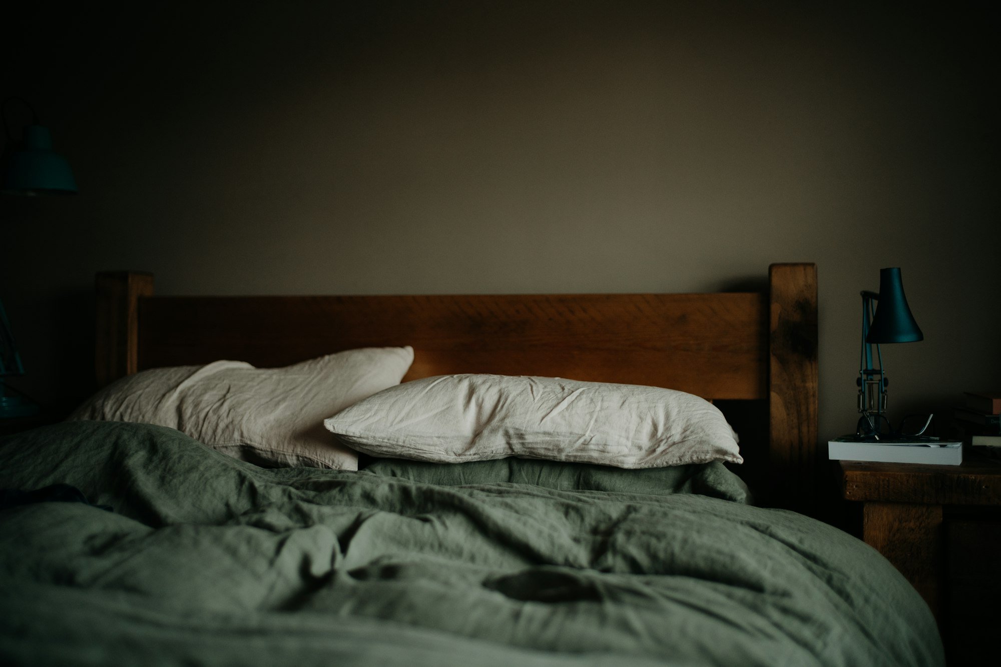 Un lit défait avec une housse de couette en lin vert sauge et des oreillers clairs