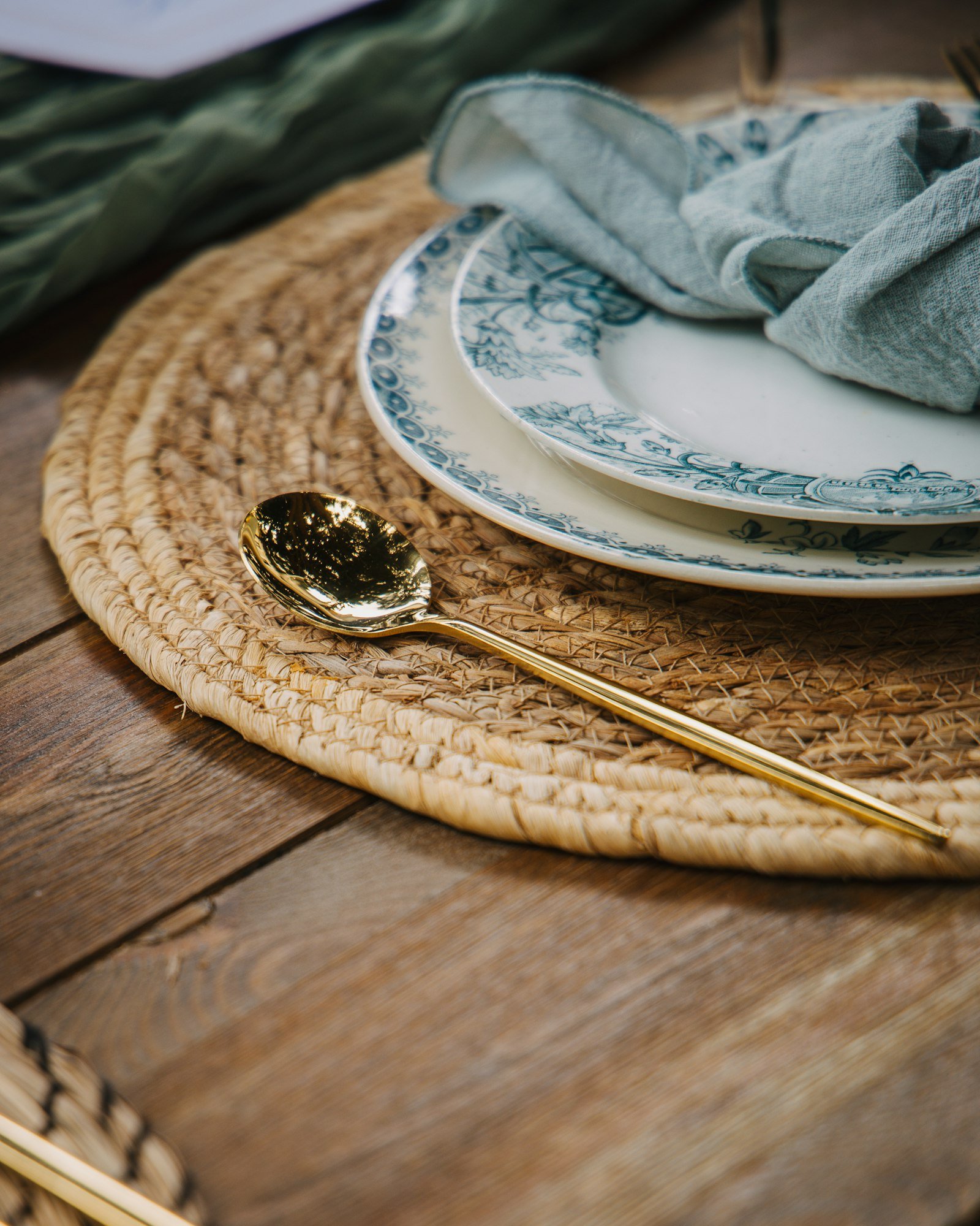 Une serviette en lin bleu-vert posée sur des assiettes, sur un set de table tressé
