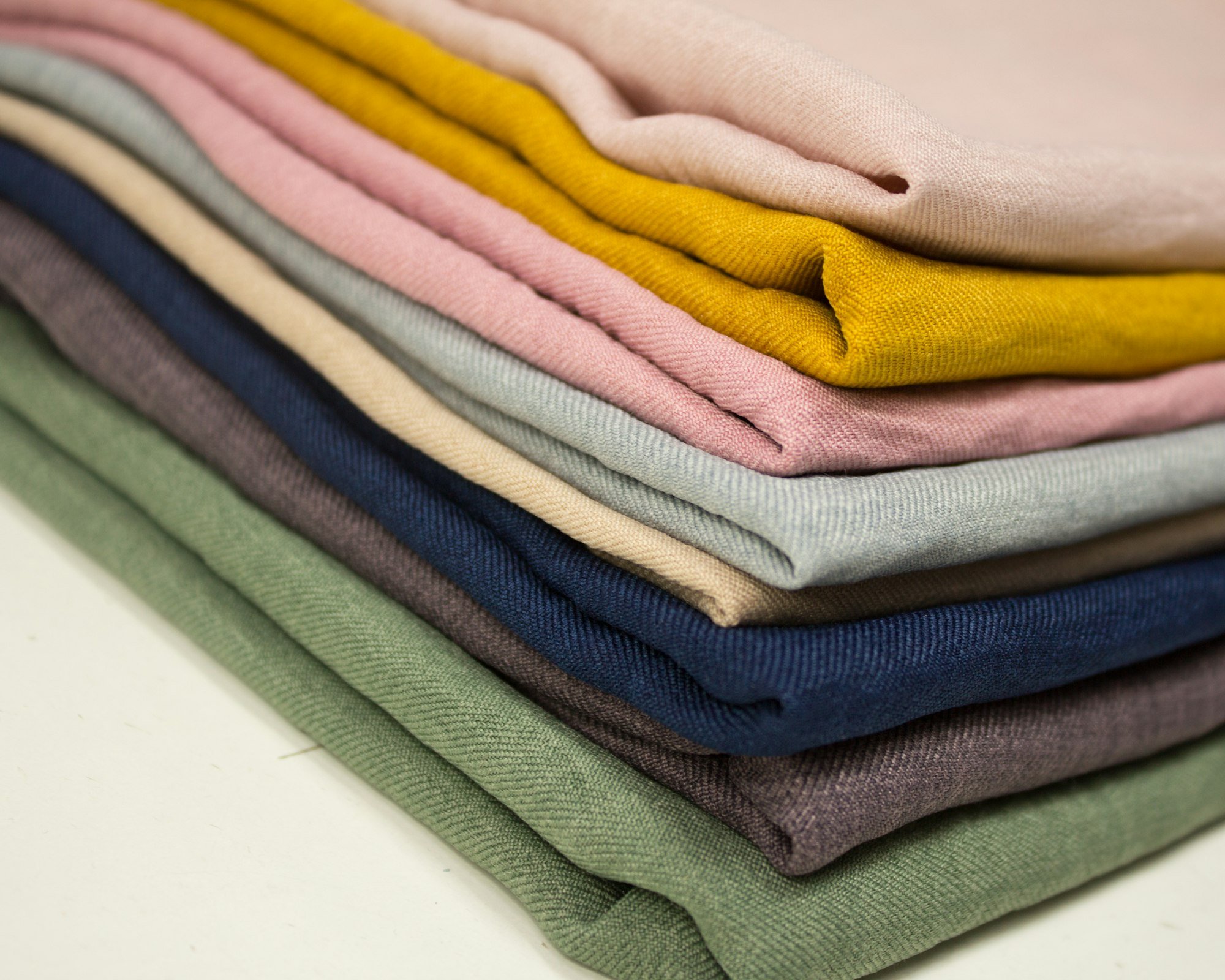 Une pile de linge en lin lavé, plié, dans des tons de sauge, bleu, rose et moutarde