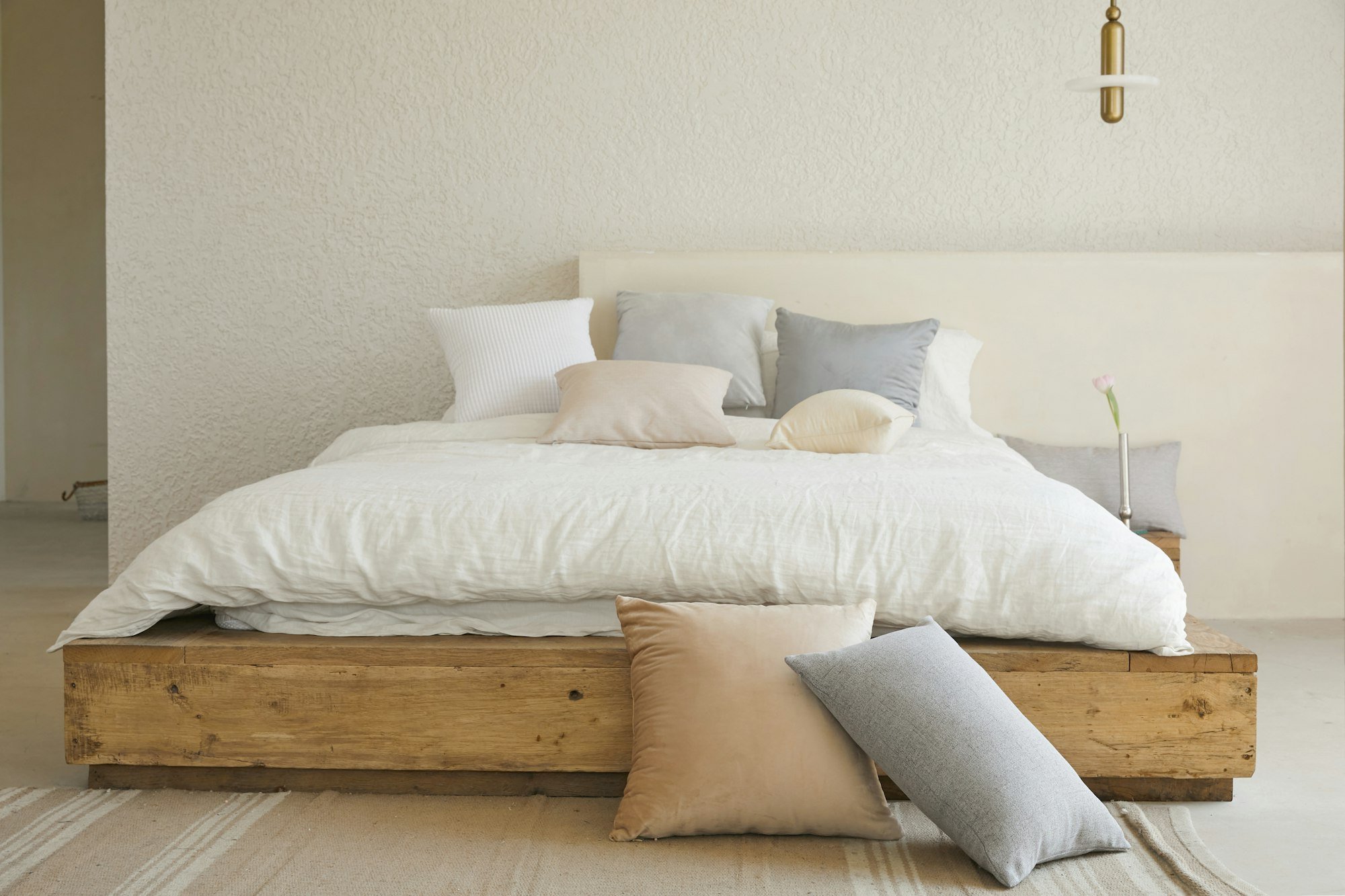 Un lit en bois clair habillé de lin naturel et de coussins, dans une chambre lumineuse