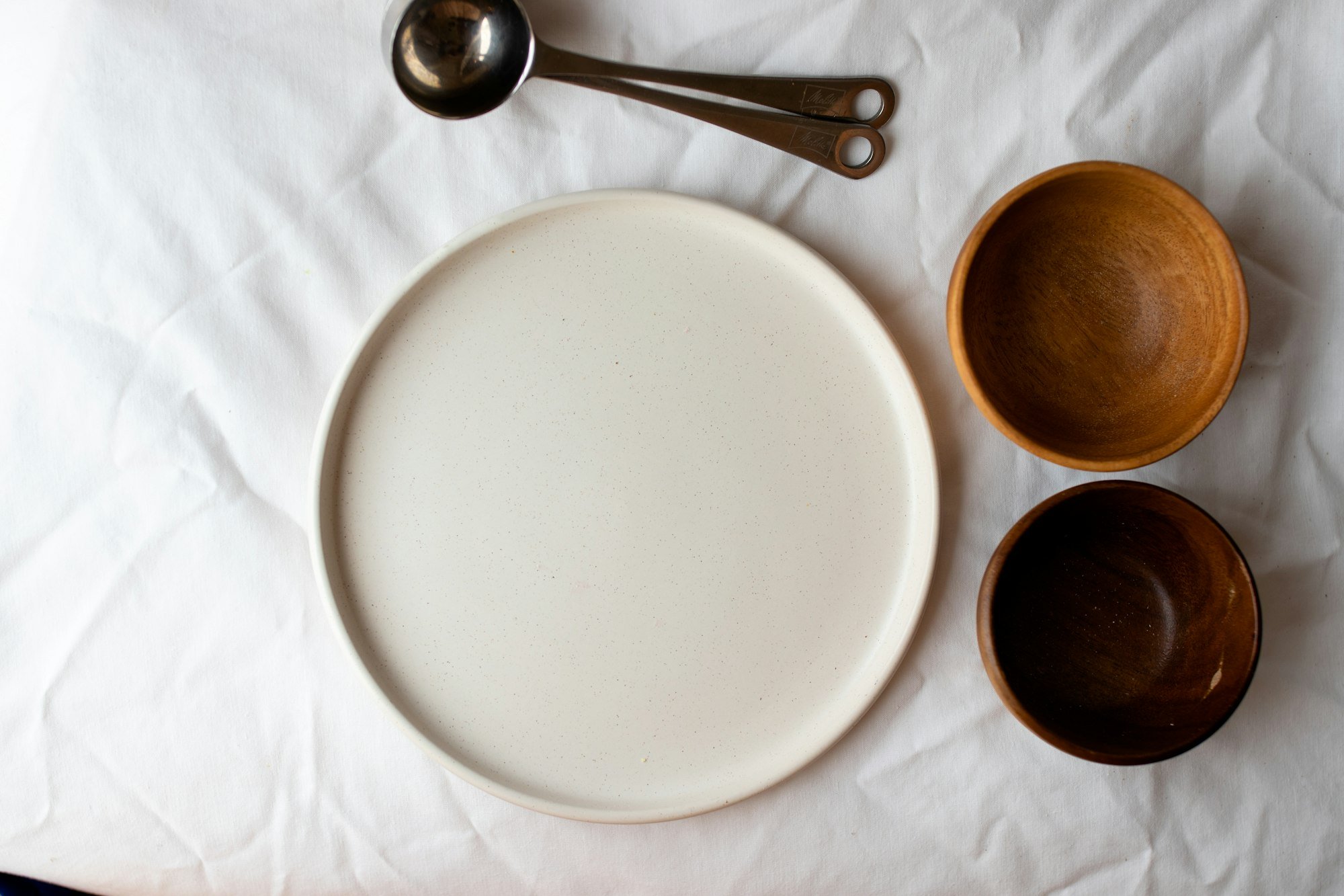 Une assiette en grès clair et deux petits bols bruns sur une nappe blanche