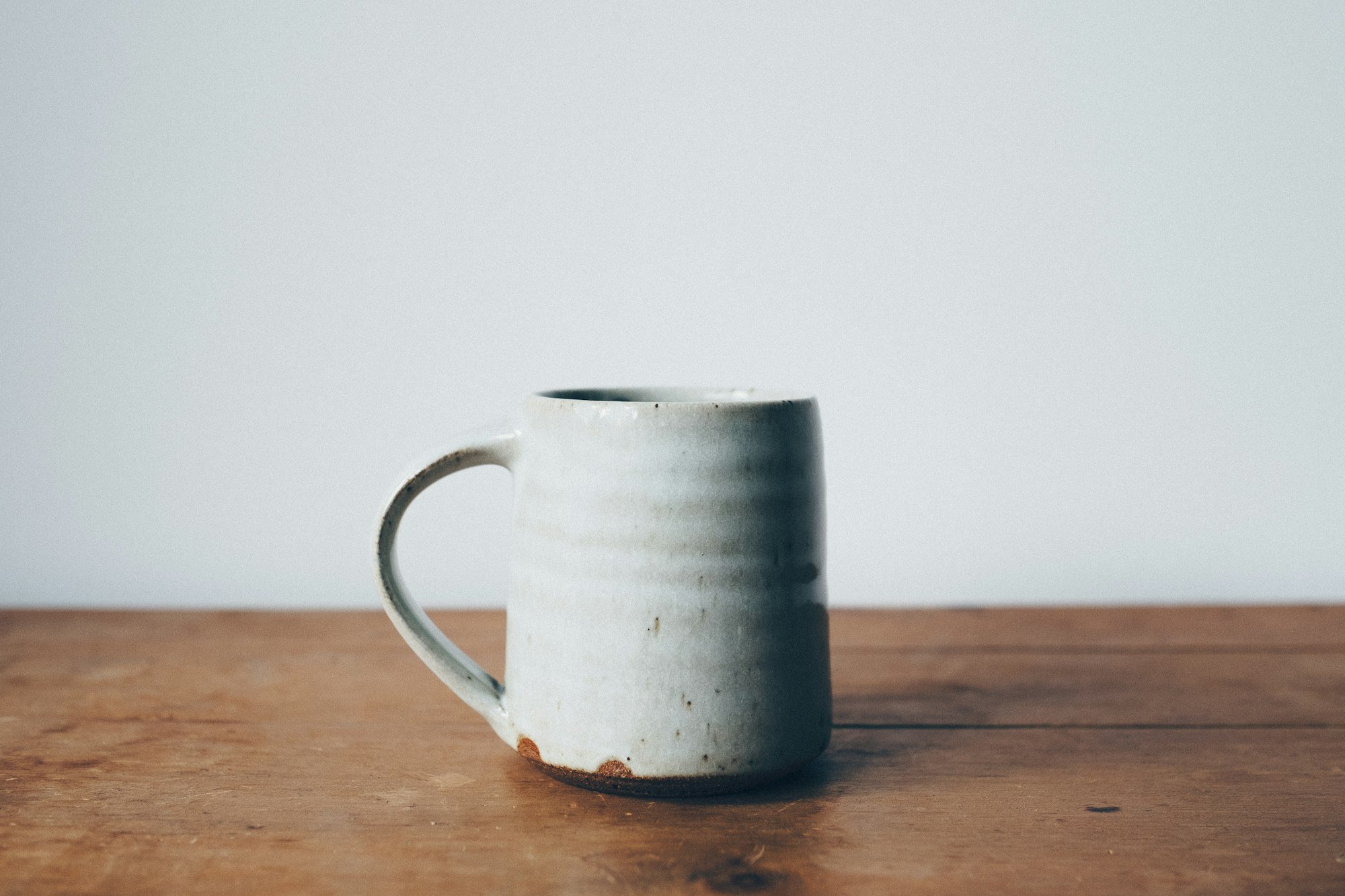 Un mug en grès à l’émail craie, posé sur une table en bois