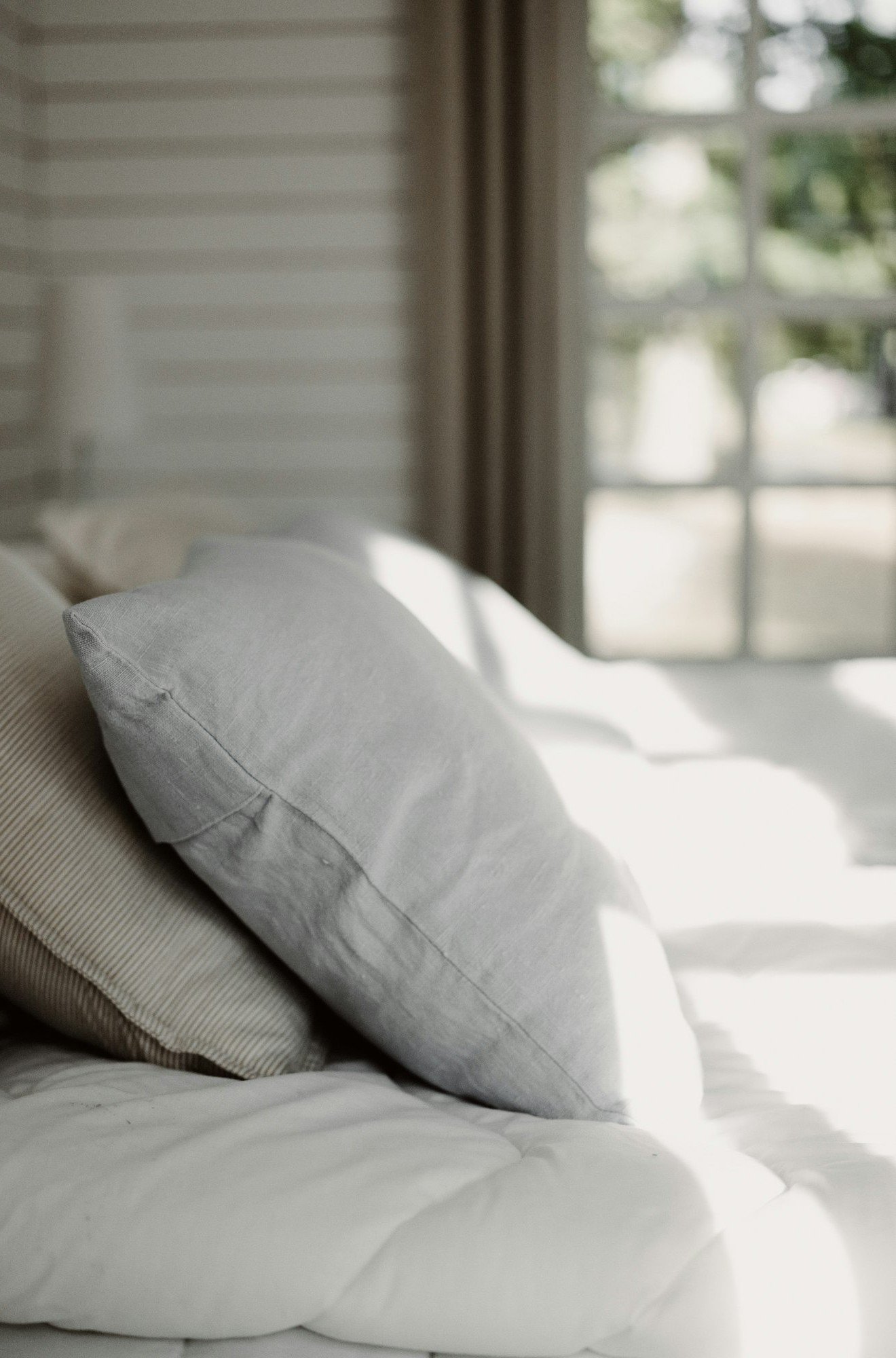 Des oreillers en lin clair sur un lit, dans la lumière du matin