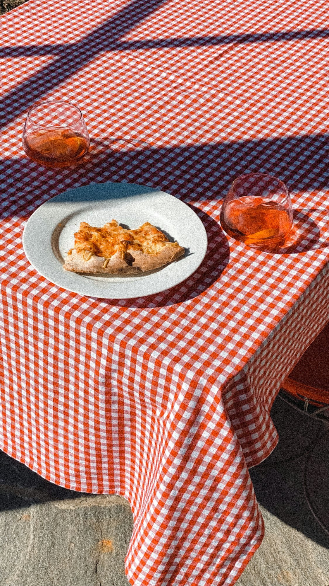 Une table dressée d’une nappe à carreaux rouges, d’une assiette et de deux verres au soleil